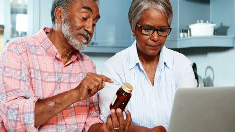 Pareja-Mayor-Sosteniendo-Un-Frasco-De-Medicina-Y-Usando-Una-Computadora-Portátil