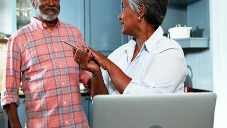 Senior-couple-talking-on-mobile-phone-in-kitchen