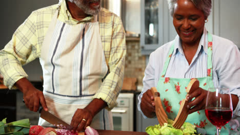 Un-Hombre-Mayor-Cortando-Verduras-Mientras-Una-Mujer-Prepara-Ensalada-En-La-Cocina