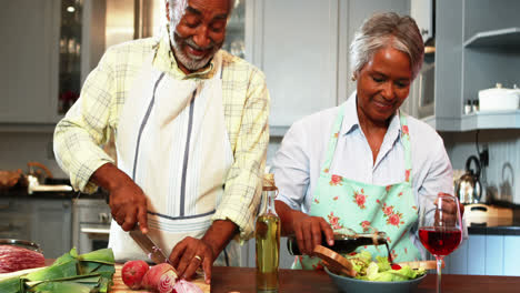 Un-Hombre-Mayor-Cortando-Verduras-Mientras-Una-Mujer-Prepara-Ensalada-En-La-Cocina