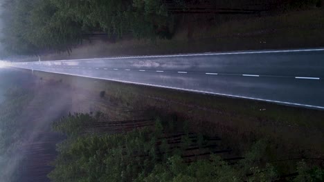 Aerial-vertical-descending-shot-over-the-asphalt-road-in-the-foggy-forest-with-mist---horror,-dark-scenery-concept