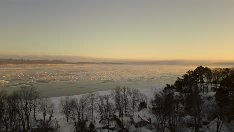 Drone-view-going-towards-the-St-Lawrence-river,-from-the-coast-of-the-Canadian-town-of-Beaumont,-Quebec,-on-a-very-cold-Winter-morning