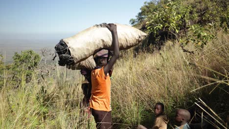 Einheimische-Kinder-In-Einem-Abgelegenen-Dorf-In-Ostafrika-Tragen-Säcke-Mit-Nahrungsmitteln-Und-Holzkohle-Auf-Dem-Kopf