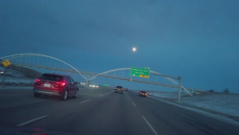 Highway-car-tilted-view-passing-under-bridge-with-full-moon-at-evening-in-Calgary,-Alberta,-Canada