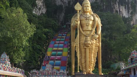 Golden-Lord-Murugan-statue-at-Batu-Caves-entrance,-colorful-stairs,-Kuala-Lumpur,-daytime