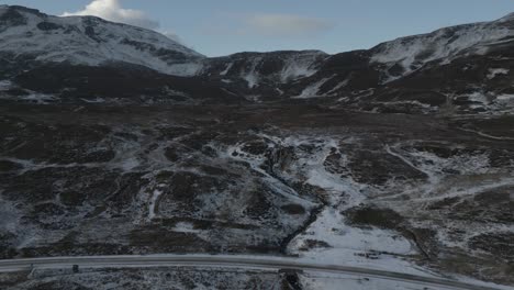 El-Icónico-Puente-Antiguo-De-Sligachan-Con-Montañas-Cuillin-Cubiertas-De-Nieve-En-Skye,-Escocia,-Cielo-Nublado,-Vista-Aérea