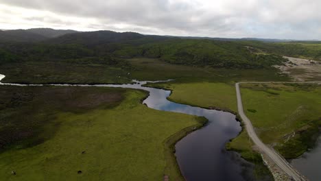 Vista-Aérea-Panorámica-De-Un-Río-Y-Montañas-Vírgenes-Con-Un-Camino-De-Tierra-Y-Un-Puente,-Día-Nublado-Cucao-Chiloe-Chile