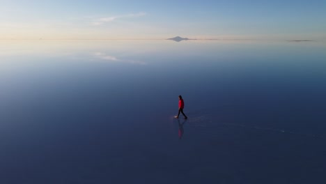 Woman-walks-on-reflective-surface-of-Uyuni-Salt-Flat,-Bolivia-aerial