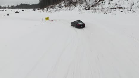 Black-car-drive-on-snowy-race-track-with-turns-near-hillside,-drift-event