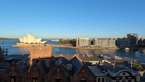 Vista-Panorámica-Lenta-Hacia-La-Izquierda-Mirando-Por-Encima-De-Los-Tejados-Hacia-Circular-Quay,-Sydney-Con-La-ópera-A-La-Luz-Del-Sol