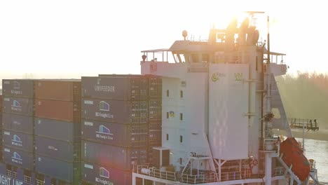 Colorful-sunrise-beyond-the-structure-of-a-container-vessel-sailing-on-a-river