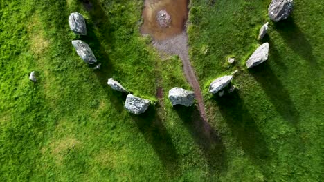 Top-down-aerial-drone-shot-rising-up-over-the-Drombeg-Stone-Circle,-an-ancient-historical-landmark-in-County-Cork,-Ireland