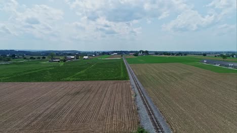 Una-Rotación-Aérea-Y-Lenta-De-Tierras-De-Cultivo,-Con-Campos-Verdes-Y-Campos-Arados-En-Un-Día-Parcialmente-Soleado.