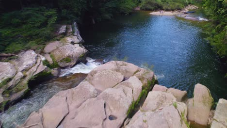 Serene-river-with-moss-covered-rocks-in-oxapampa,-peru,-with-lush-forest-backdrop,-daylight,-aerial-view