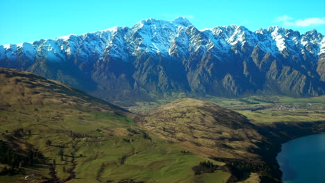 The-Remarkable's-South-Island-Queenstown-New-Zealand-snowy-mountain-peaks-green-valley-aerial-drone-winter-beautiful-sunny-morning-afternoon-Lake-Wakatipu-Wanaka-landscape-to-the-right-movement