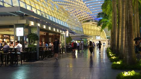 People-strolling-and-jogging-along-the-waterfront-promenade-in-the-evening,-people-dining-at-outdoor-restaurants-and-bars-at-The-Shoppes-Marina-Bay-Sands,-Singapore