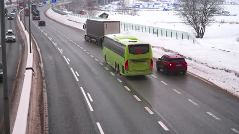 A-trailer-truck-merging-in-front-of-a-green-Ruter-bus-on-the-E18-motorway,-heading-away-from-camera