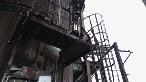Estructura-Industrial-Abandonada-Y-Oxidada-Con-Una-Escalera-De-Caracol-Adjunta-A-Su-Lado