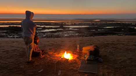 Eine-Gruppe-Von-Menschen-Steht-Um-Das-Lagerfeuer,-Camping-Am-Meer,-Versammlung-Um-Ein-Heißes,-Warmes-Lagerfeuer,-Sonnenaufgangszeit,-Kalter-Früher-Morgen-Auf-Der-Insel-Qeshm,-Reise-Zum-Meeresabenteuer,-Wassersport,-Surfen,-Yachtclub