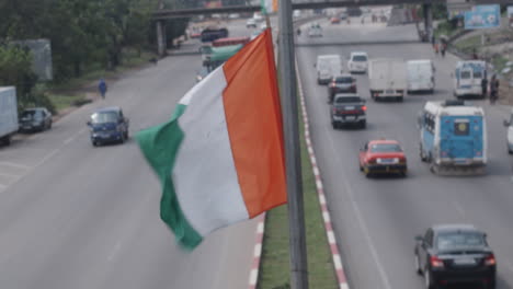 Primer-Plano-De-Una-Bandera-De-Costa-De-Marfil-Ondeando-En-Un-Poste-En-Medio-De-La-Carretera.