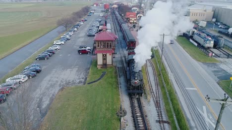 An-Aerial-View-of-a-Train-Station,-with-a-Steam-Passenger-Train,-Disconnecting-from-the-Coaches,-Blowing-Smoke,-on-a-Partially-Sunny-Day