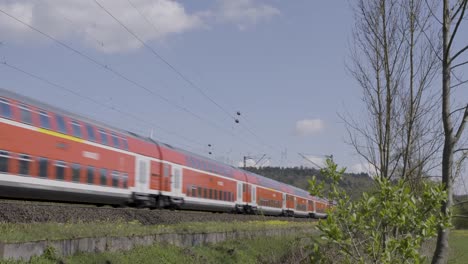 Orange-Deutsche-Bahn-train-speeding-through-a-rural-landscape-with-wind-turbines-in-the-background,-daylight