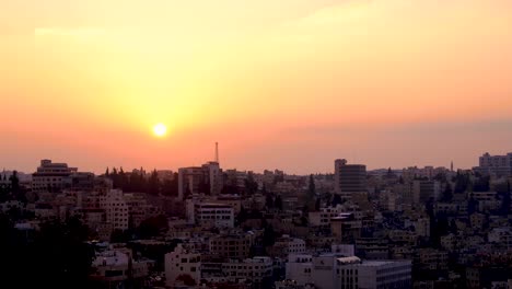 Panoramic-landscape-view-of-beautiful-golden-sunset-sky-with-sun-dipping-over-densely-populated-buildings-of-urban-skyline-in-Jordanian-capital-city,-Middle-East