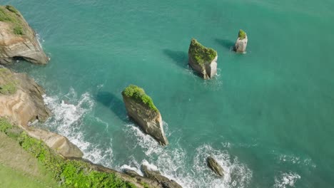 Three-Sisters-rock-columns-standing-tall-at-shore-of-New-Zealand,-drone-shot