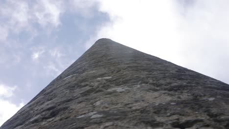 A-close-up-shot-looking-up-at-the-tall-Round-Tower-at-Glendalough,-dollying-around-the-base-of-the-ancient-landmark-in-Wicklow,-Ireland