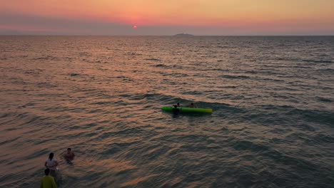 Aerial-view-showing-people-in-water-swimming-and-having-fun-with-kayak-at-sunset