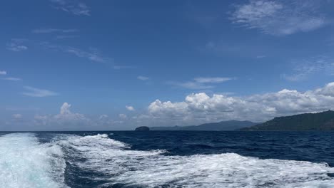 White-waves-splashing-as-traveling-on-a-motor-boat-with,-green-lush-islands-in-the-background