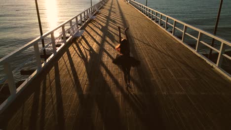 Woman-dancer-expressing-ballet-steps-on-beach-pier-at-sunset
