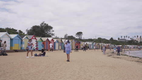 Turistas-De-Vacaciones-En-La-Playa-De-Brighton-Con-Coloridas-Cajas-De-Baño-En-Melbourne,-Australia