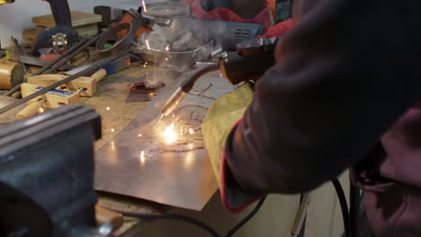 Close-up-of-a-man's-hands-working-with-a-welder-on-metal-on-a-messy-workshop