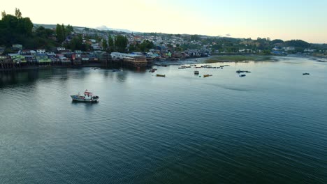 Bird's-eye-view-establishing-on-the-Castro-stilt-houses-on-the-island-of-Chiloé-with-seagulls-and-fishing-boats-on-the-shore,-sunset-in-southern-Chile