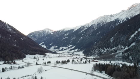 Una-Vista-Aérea-De-Montañas-Nevadas-Con-Una-Carretera-Que-Atraviesa-El-Centro-De-Un-Valle-Alpino-En-Italia