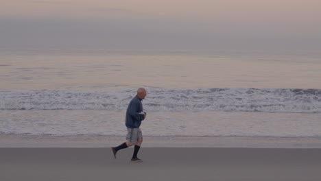 Weißer-Mann-Mittleren-Alters-Joggt-In-Zeitlupe-Am-Strand-Mit-Dem-Pazifischen-Ozean-Im-Hintergrund-In-Venice-Beach,-Kalifornien