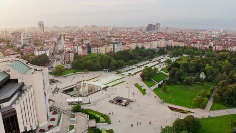 Many-skateboarder-in-famous-park-in-Sofia,-Bulgaria,-aerial-establisher-skyline