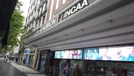 Entrance-Facade-of-Gamumont-Cinema-Public-Showcase-at-Buenos-Aires-City-Daylight-Argentina,-Congreso-Neighborhood,-People-Walk-Urban-Landscape-with-Trees