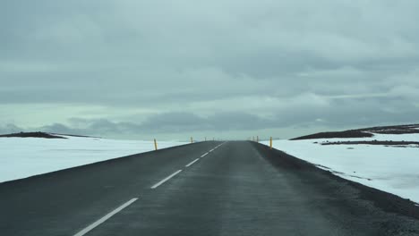 Icelandic-road-stretching-into-the-horizon,-snowy-landscape-on-both-sides,-overcast-sky,-first-person-view-from-car