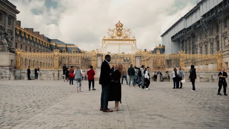 Una-Pareja-De-Raza-Mixta-Frente-Al-Famoso-Castillo-De-Versalles,-El-Odio-Principal-Dorado-Del-Honor-En-París,-Francia,-Abrazándose-Y-Coqueteando-En-Un-Día-Nublado-De-Primavera:-Plano-Cinematográfico-Amplio