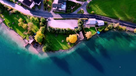 Pueblo-Alpino-Bañado-Por-El-Sol-Enclavado-En-Un-Valle-Verde,-Casas-Coloridas-Con-Techos-De-Terracota-Se-Agrupan-Alrededor-De-Un-Lago-Azul-Brillante