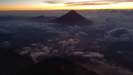 Aerial-orbit-over-Guatemala's-volcanoes-at-sunrise,-revealing-Fuego's-glowing,-lava-filled-crater-during-vibrant-golden-hour-just-before-sunrise