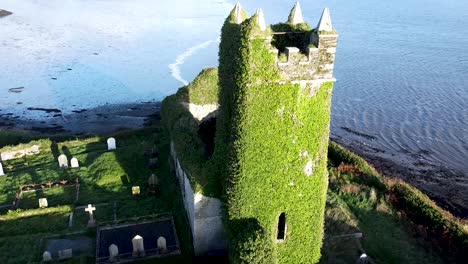 Toma-Aérea-De-Un-Dron-De-Las-Ruinas-De-La-Iglesia-De-San-Mateo-En-El-Cementerio-De-Aughadown,-Desplazándose-Para-Revelar-El-Hermoso-Río-Ilen-Que-Rodea-El-Monumento-Histórico.