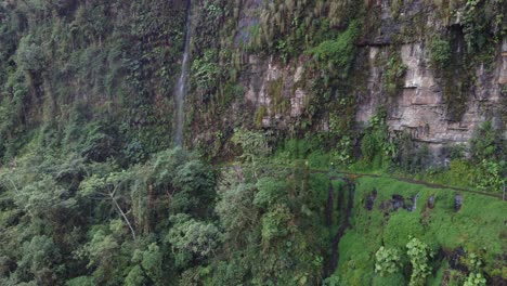 Cyclist-nears-waterfall-on-narrow-section-of-Yungas-Rd-Bolivia,-aerial