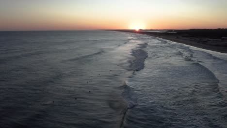 Vista-Aérea-De-Surfistas-En-El-Océano-Al-Atardecer,-Esperando-Olas-En-Una-Tarde-Tranquila