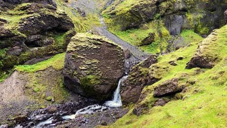 Rocky-mossy-landscape-and-small-flowing-river-with-waterfall-in-Iceland,-handheld