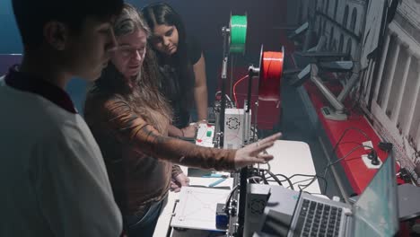 Still-shot-of-a-Caucasian-female-teacher-teaching-a-male-and-another-female-student-how-to-use-a-3D-printer-connected-to-a-laptop