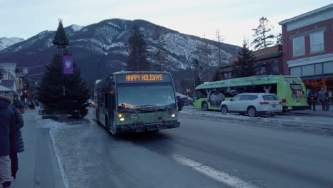 Electric-Buses-in-service-on-street-pulling-into-bus-station-at-evening-in-downtown-Banff,-Alberta,-Canada