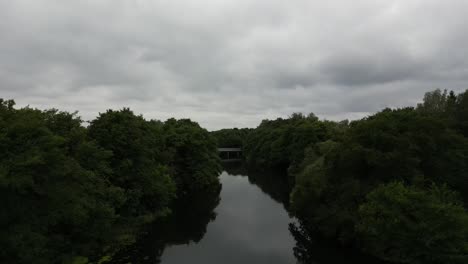 Drone-recording-of-the-Gudenå-River,-flies-over-and-along-the-stream-on-its-way-to-a-small-bridge,-the-drone-continues-over-the-bridge-and-finally-shows-a-beautiful-landscape